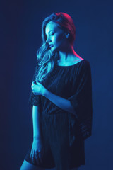 Beautiful ,young blonde with bright scarlet lips and expressive eyes in a black jumpsuit in neon light blue and red lamps.