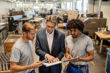 Young metal workers cooperating with their manager while reading reports in a factory.
