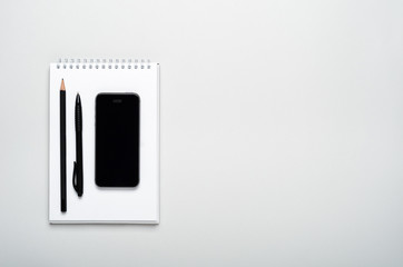 Smartphone, pencil, pen on a notepad on a gray background. Office desktop, minimal composition. Copy space, top view, flat lay.