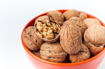 pile of walnuts lying in an orange bowl on a white background