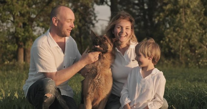 Happy family with a dog in nature. 7 year old boy with his parents petting a dog breed German shepherd. Smiling family on the field with dog. People are with his pet in the meadow. Slow motion