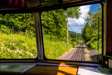 A view from the window of a moving train, visible tracks, trees and blue sky with white clouds.