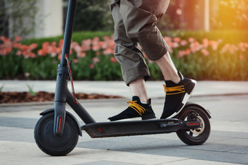 Close up of man riding black electric kick scooter at beautiful park landscape