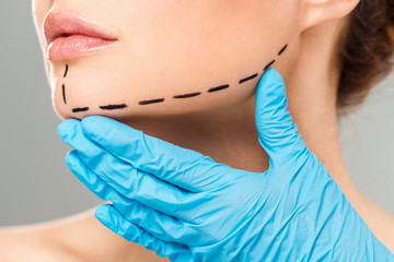 cropped view of plastic surgeon touching face of woman with marked face isolated on grey