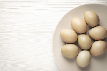 Top view pheasant eggs in a white dish on a white wooden table with copy space