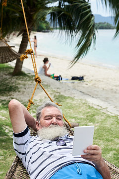 Man resting in a hammock and reading ebook at the beach. Holidays,
