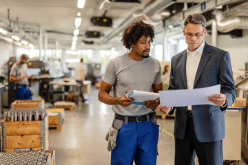 Fototapeta na wymiar Businessman and African American worker reading project plans in factory plant.