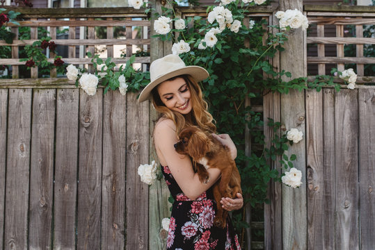 A woman in her twenties walking her puppy down the street in the summer time.