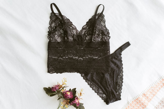 black lace underwear is lying on the light bed. Home erotic lingerie lies on a light background next to the flowers. Home clothes without anyone.