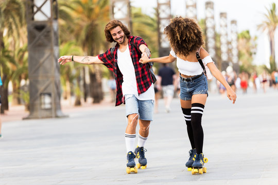 Beautiful young couple skating with rollerblades in the street.