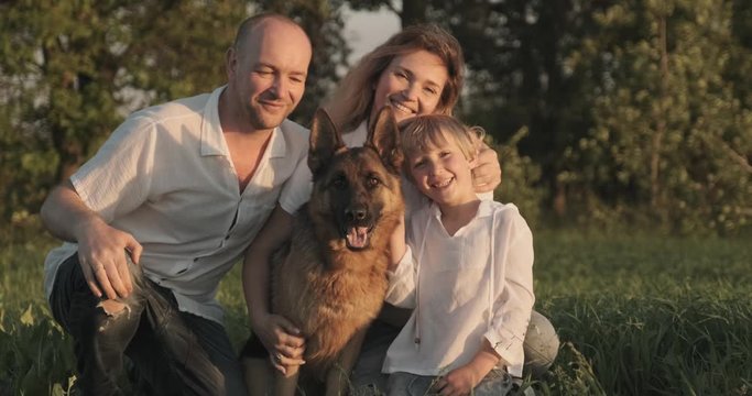 Happy family with a dog in nature. 7 year old boy with his parents petting a dog breed German shepherd. Smiling family on the field with dog. People are with his pet in the meadow. Slow motion
