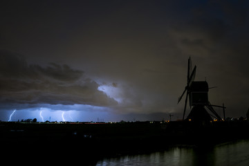 Three lightning bolts next to each other hit the ground during a severe thunderstorm near the city of Leiden in The Netherlands. A classic dutch windmill stands in the foreground.
