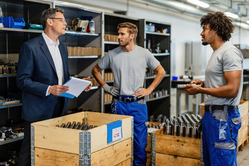 Quality control inspector and manual workers communicating wile standing by crates full of steel...