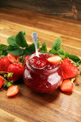 strawberry jam with fresh strawberries and mint. marmalade on spoon and jar on brown wood