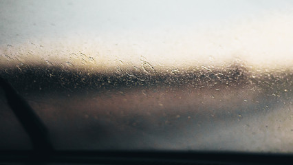 wipers and washers in raining day. View from car seat. Blur Background at sunset. Drops of rain on car window pane. Blurred droplet on car window wiper glass raindrops. Driving in rain weather.