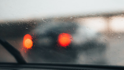 Abstract car window in raining day. View from car seat. Blur Background of Blurred Drops of rain on car window pane, sun light over empty road. Driving in rain weather.