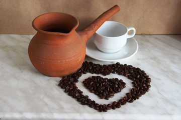 brown clay Turk for cooking Arabic coffee, white Cup and saucer and roasted coffee beans in the shape of a heart, selective focus