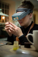 Female jeweler looking at gold through headband magnifier in workshop