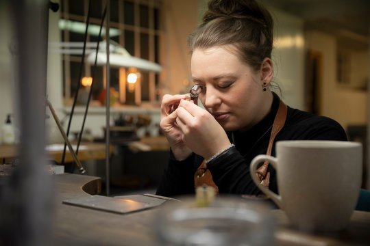 Female Jeweler Examining Gold Through Loupe At Workshop