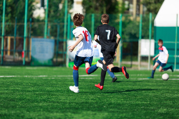 Boys at blue white sportswear run, dribble, attack on football field. Young soccer players with ball on green grass. Training, football, active lifestyle for kids	