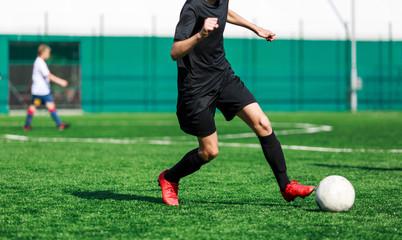 Boys in white and black sportswear plays  football on field, dribbles ball. Young soccer players with ball on green grass. Training, football, active lifestyle for kids concept 