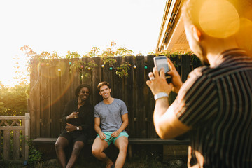 Man tar bild pÂ v‰nner pÂ b‰nk i tr‰dgÂrd med smartphone