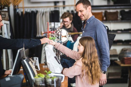 Side view of daughter receiving shopping bag from cashier by father at checkout counter in clothing store