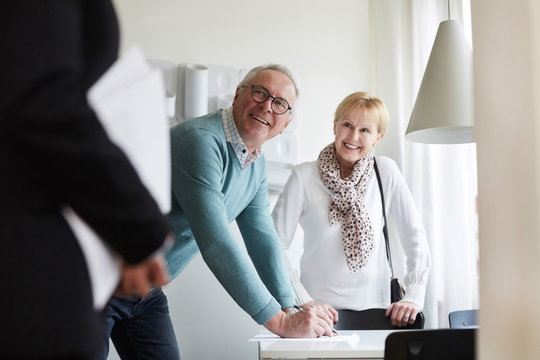 Smiling senior couple looking at real estate agent while signing for new house