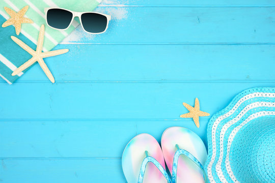Beach accessories on a blue wood background. Summer vacation concept border with copy space. Sunglasses, sea shells, towel, flip flops and striped hat.