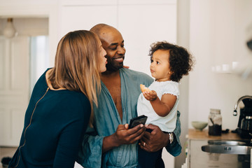 Smiling mother and father looking at daughter eating biscuit while carrying her at home