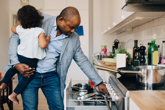 Father carrying daughter while looking at utensils in kitchen
