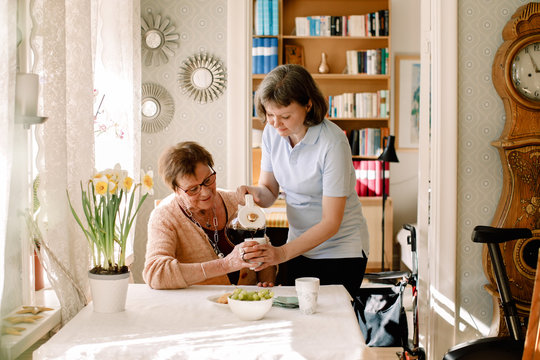 V&Acirc;rdpersonal h&permil;ller upp kaffe till kvinna vid matbord