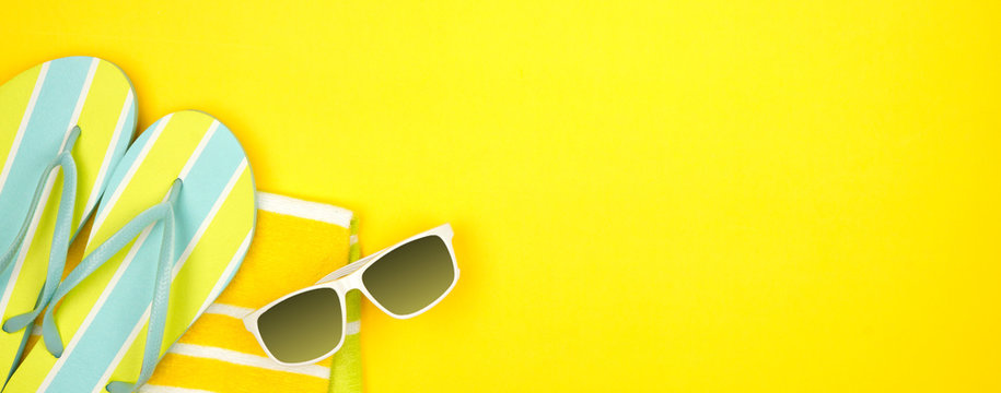 Beach accessories on a yellow background. Summer vacation concept banner with copy space. Sunglasses, towel and flip flops.