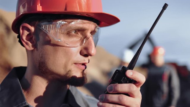 Close-up face male engineer in glasses and helmet talking using walkie talkie at construction site