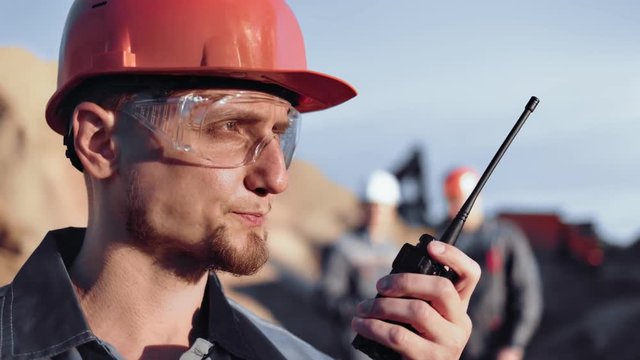 Skilled male construction engineer in uniform reporting using walkie talkie during working close-up