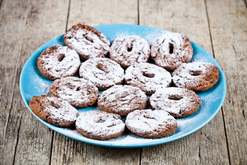 Fresh baked chocolate chip cookies with sugar powder on blue plate on rustic wooden table.