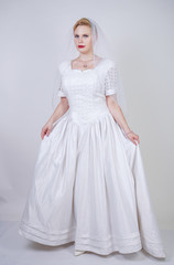 pretty curvy adult woman with short hair wearing long vintage wedding dress with sun style skirt. young caucasian bride with veil on white studio background alone.