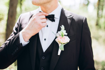 the groom in a suit straightens his tie bubochku. boutonniere on the lapel of his jacket. young man in a business suit.