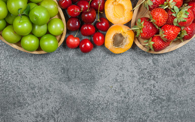 Summer fruits, green plum, red cherry, strawberry, apricot on grey rustic table. top view, copy space for text, selective focus