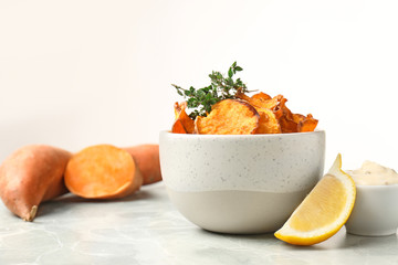 Bowl of sweet potato chips with sauce and lemon on table against white background. Space for text