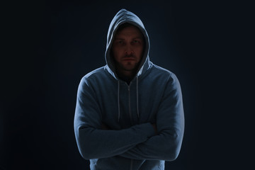 Mysterious man in hoodie on dark background. Dangerous criminal