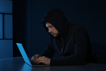 Man using laptop in dark room. Criminal offence