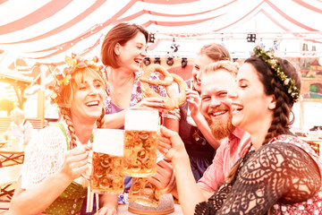 5 Freunde in Gruppe beim Biertrinken im Festzelt haben Spaß in Trachten und Dirndl und Lederhosen 