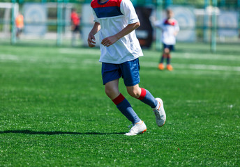 Fototapeta premium Boys at blue white sportswear run, dribble, attack on football field. Young soccer players with ball on green grass. Training, football, active lifestyle for kids