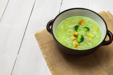 Bowl of broccoli cream soup on white wooden table. Image with copy space
