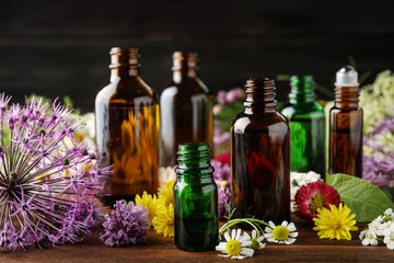 Different bottles of essential oils and flowers on table