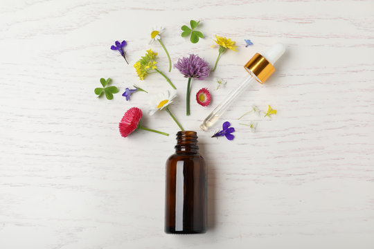 Bottle of essential oil and different flowers on white wooden background, flat lay