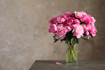 Fragrant peonies in vase on table against color background, space for text. Beautiful spring flowers