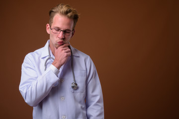 Young handsome man doctor against brown background
