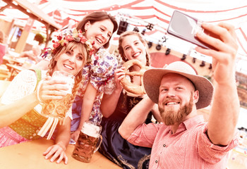 Freunde in Trachten mit Dirndl und Lederhose im Bierzelt am Biertisch machen Selfie Gruppenfoto